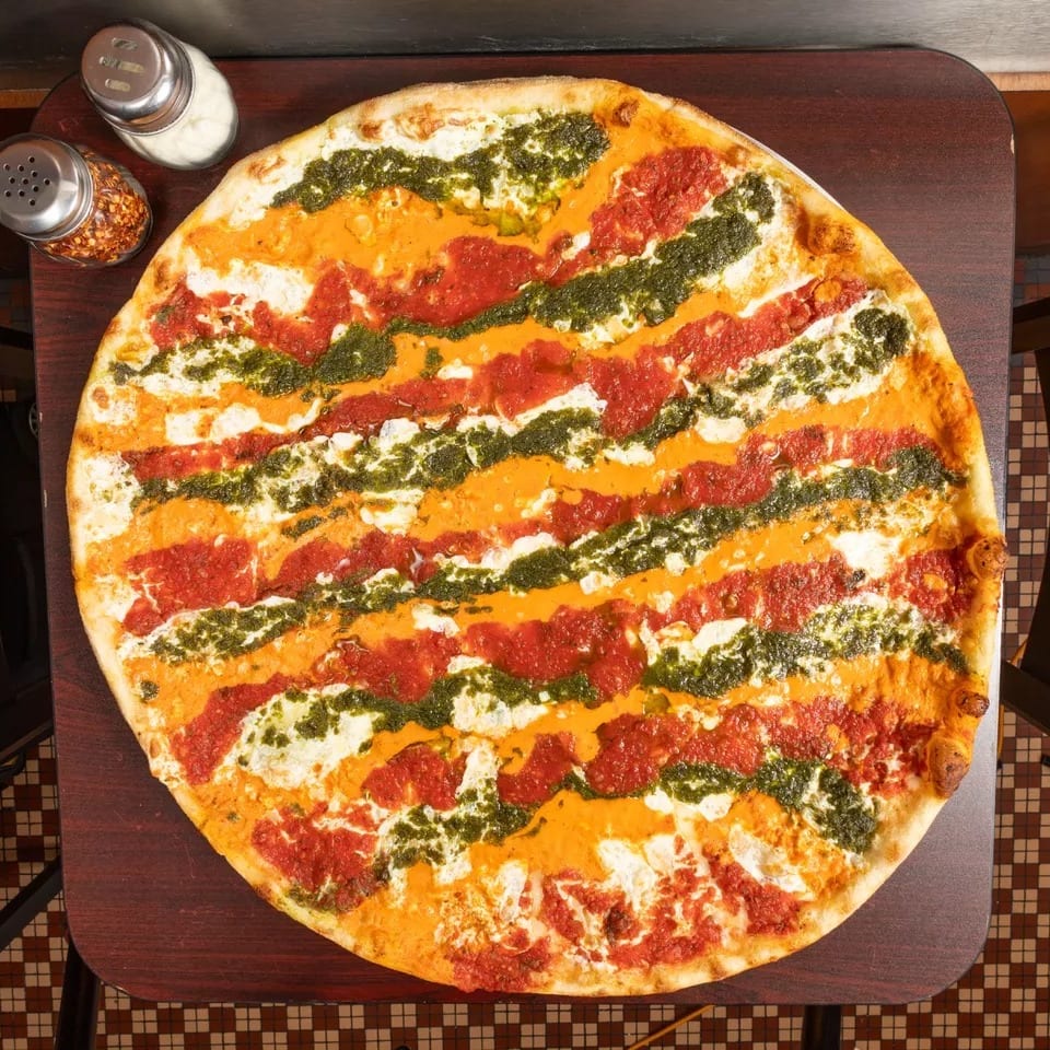 Overhead view of a large pizza with stripes of red sauce, orange vodka sauce, and green pesto.