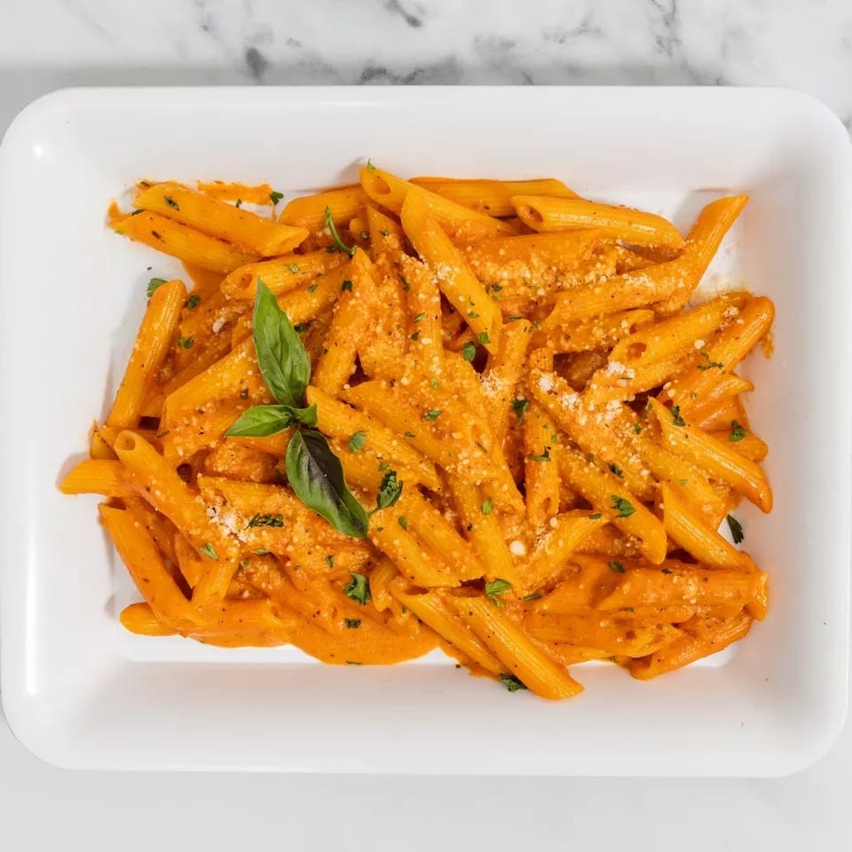 Penne pasta in a creamy orange sauce, garnished with fresh basil and grated cheese.