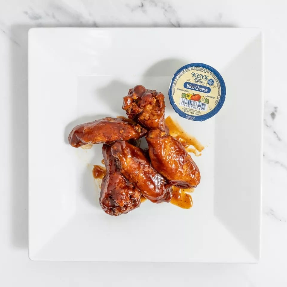 Four saucy chicken wings on a white plate with a side of Ken's Bleu Cheese dressing.