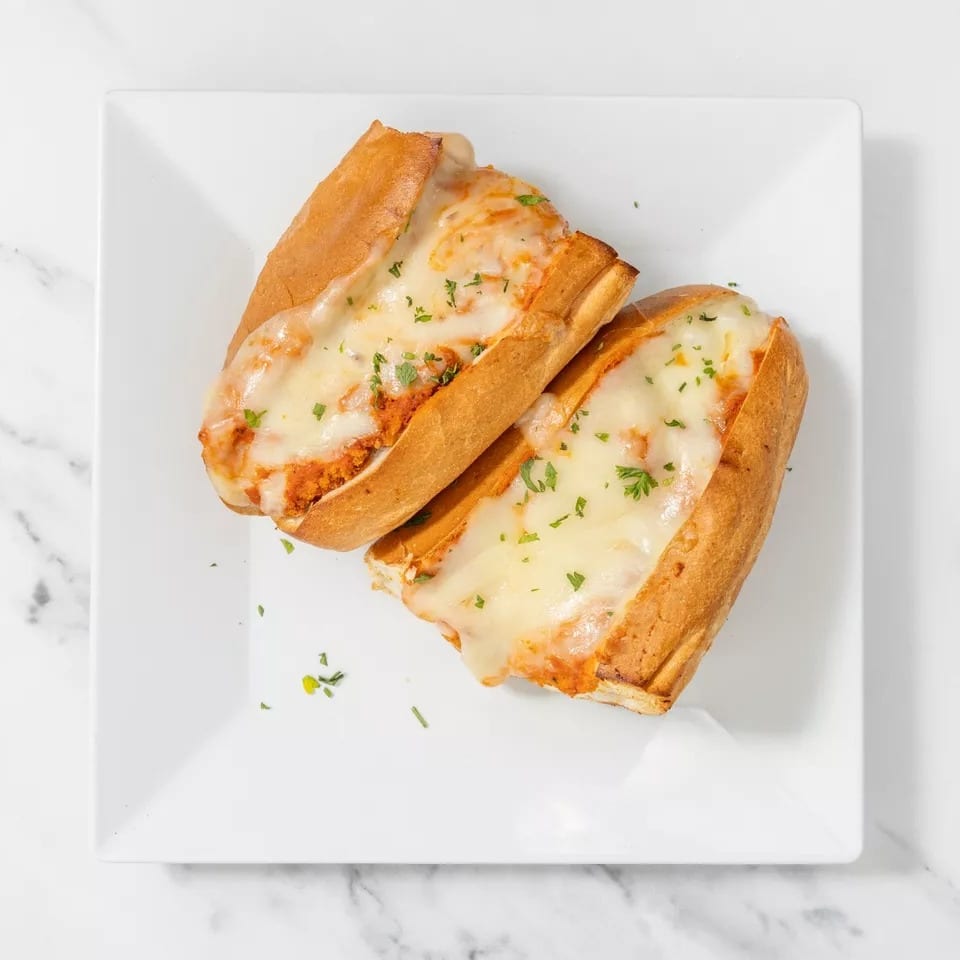 Two cheesy meatball subs on a white rectangular plate, garnished with parsley.