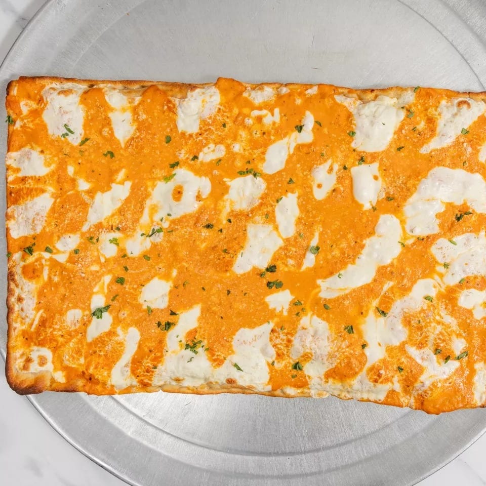 Rectangular pizza with orange sauce and white cheese swirls, garnished with herbs on a metal tray.